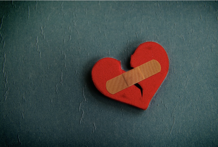 Torn red felt heart on dark gray background patched with a bandage