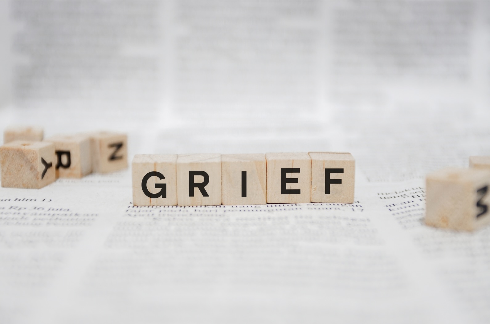 Wooden blocks spell GRIEF on newsprint background